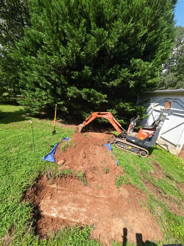 Soil dug away with a mini excavator to expose the top of an old homemade septic tank
