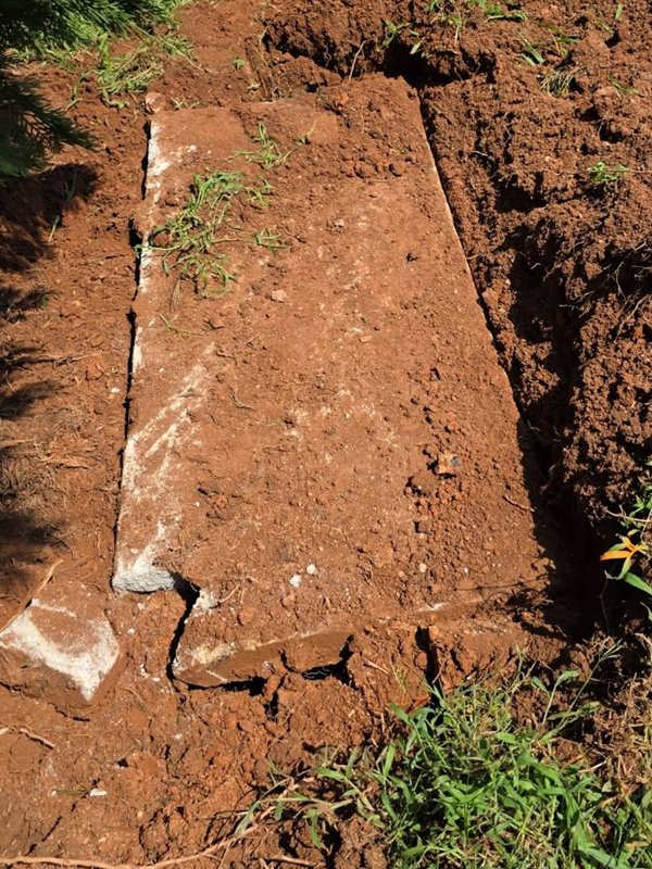 Cracked concrete slab lid of a homemade septic tank, uncovered in red clay