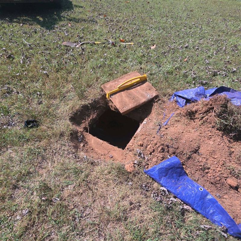Septic tank with its lid removed and set beside the opening, with a lid lifter on top
